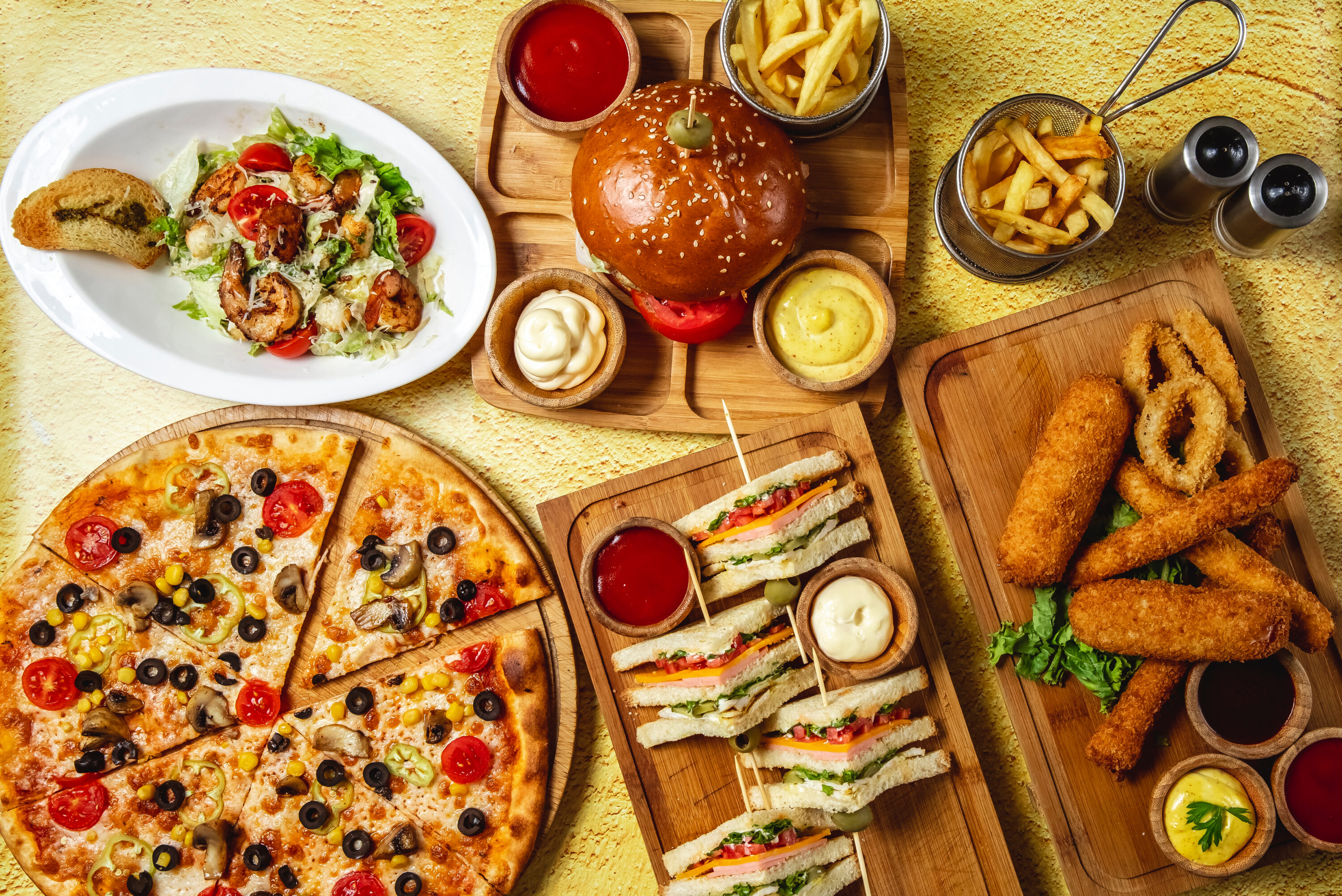 fast-food-mix-mozzarella-sticks-club-sandwich-hamburger-mushroom-pizza-caesar-shrimp-salad-french-fries-ketchup-mayo-and-cheese-sauces-on-the-table
