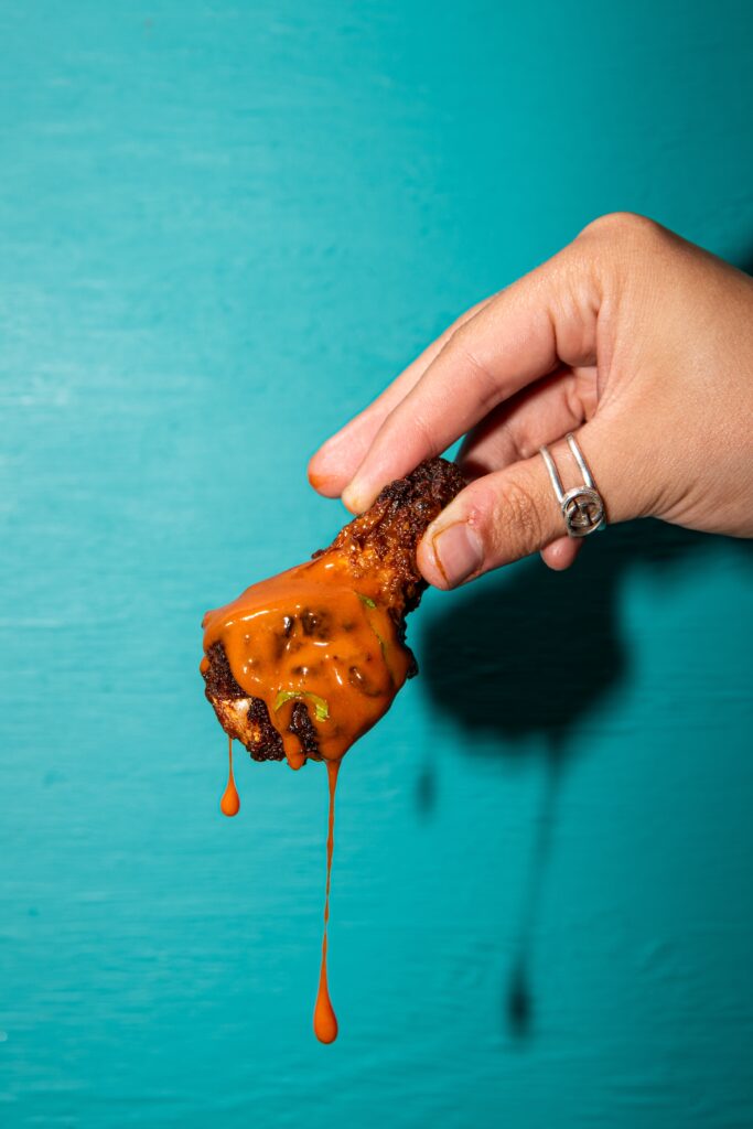 hand-holding-flavorful-american-tapas-chicken-wings-with-sauce-dripping