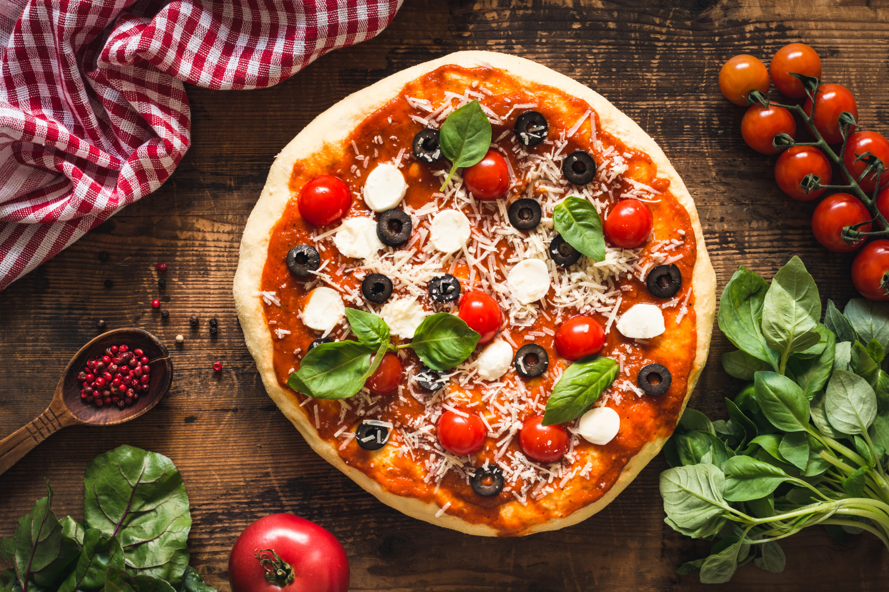 Pizza with sauce, tomatoes, olives, basil and cheese.