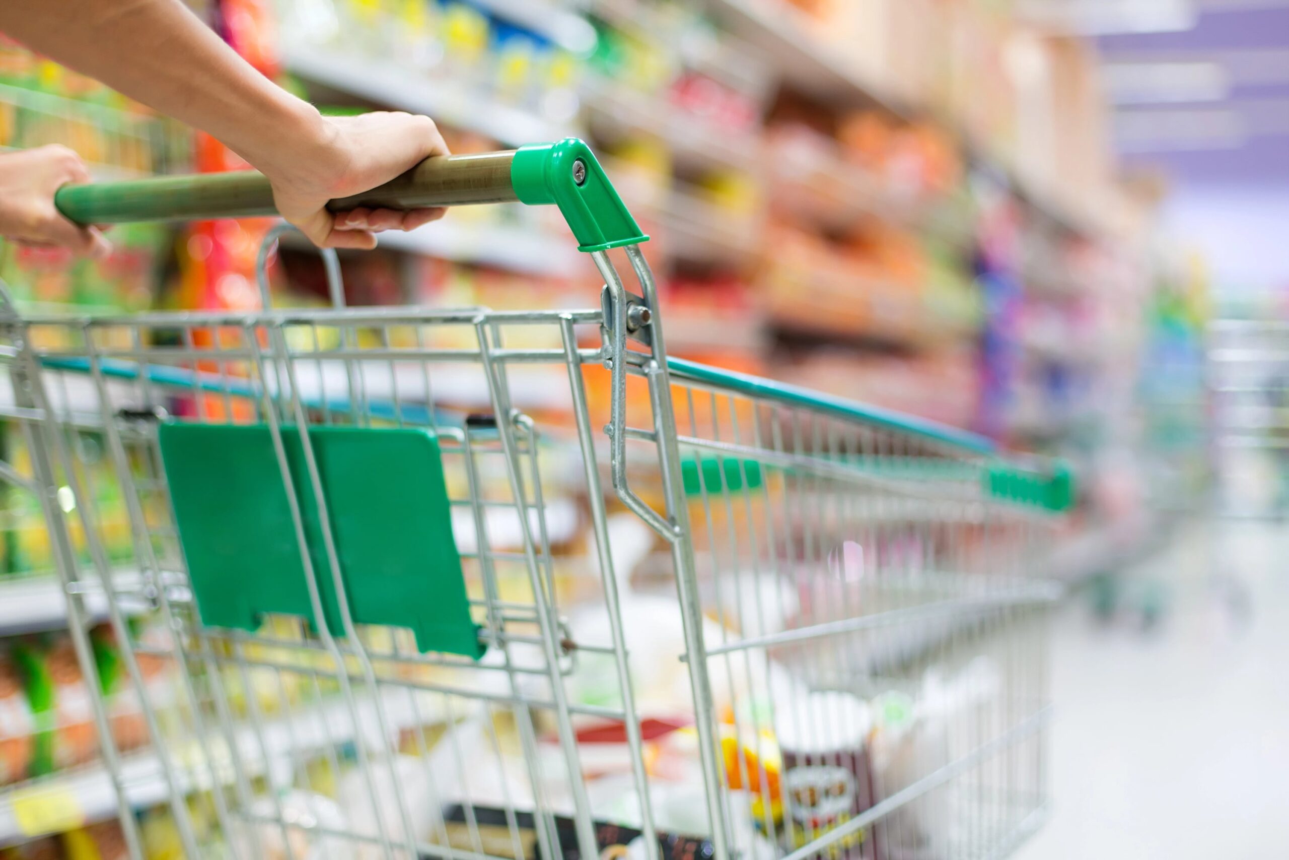 Close-up of hands on grocery cart in store aisle