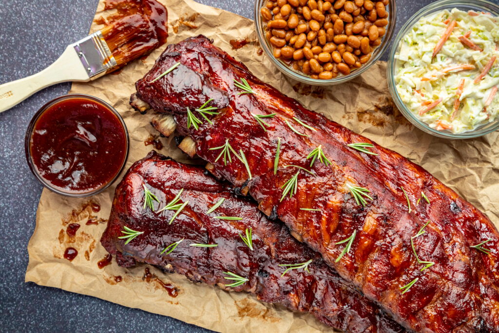 Barbecue sauce beside bbq ribs, beans, coleslaw