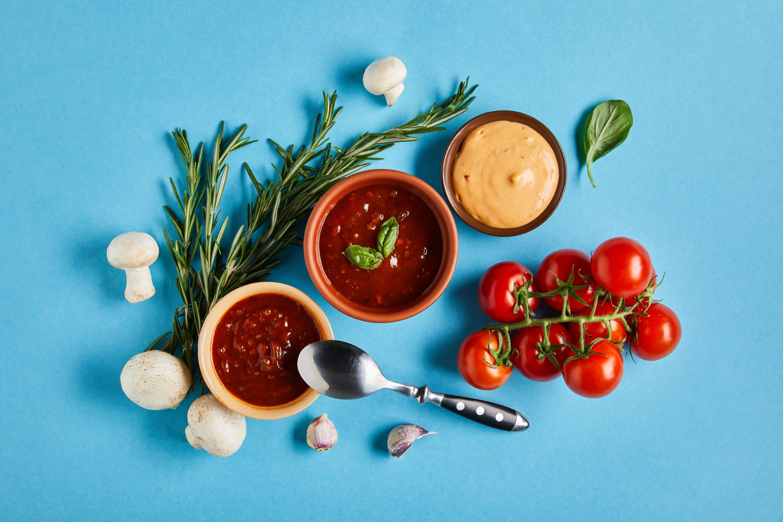 Three sauces in small bowls, tomatoes, rosemary, mushrooms, garlic