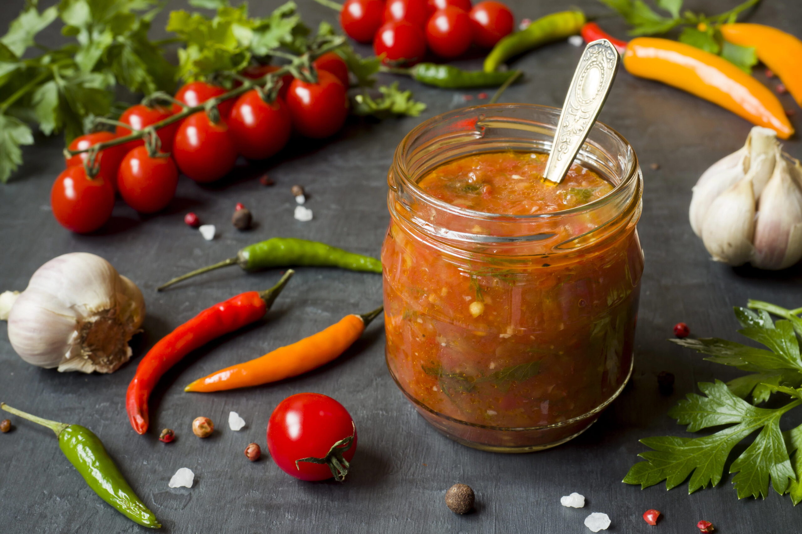 Jar of sauce surrounded by garlic, peppers, tomatoes, herbs