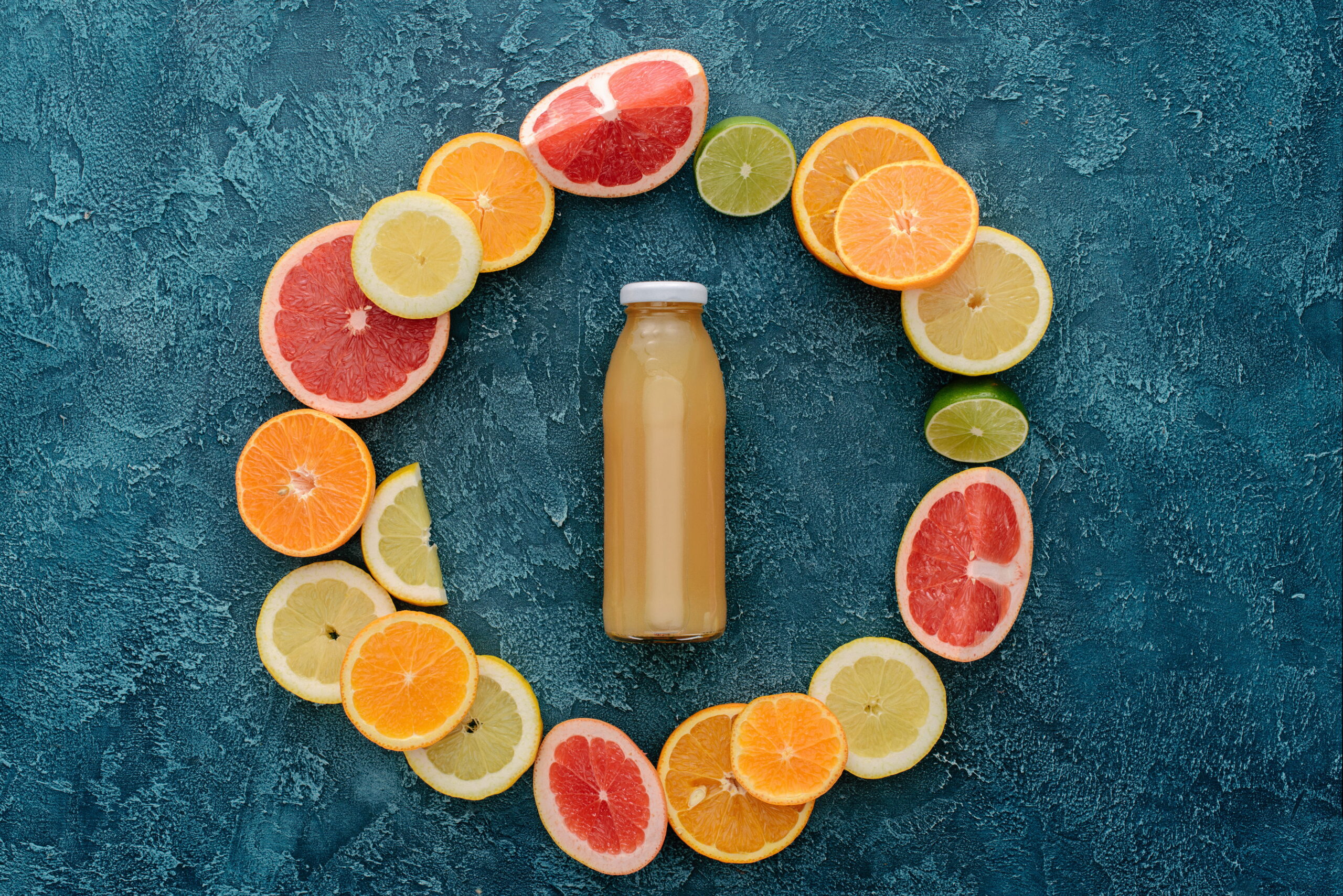 Orange bottled beverage surrounded by citrus fruit