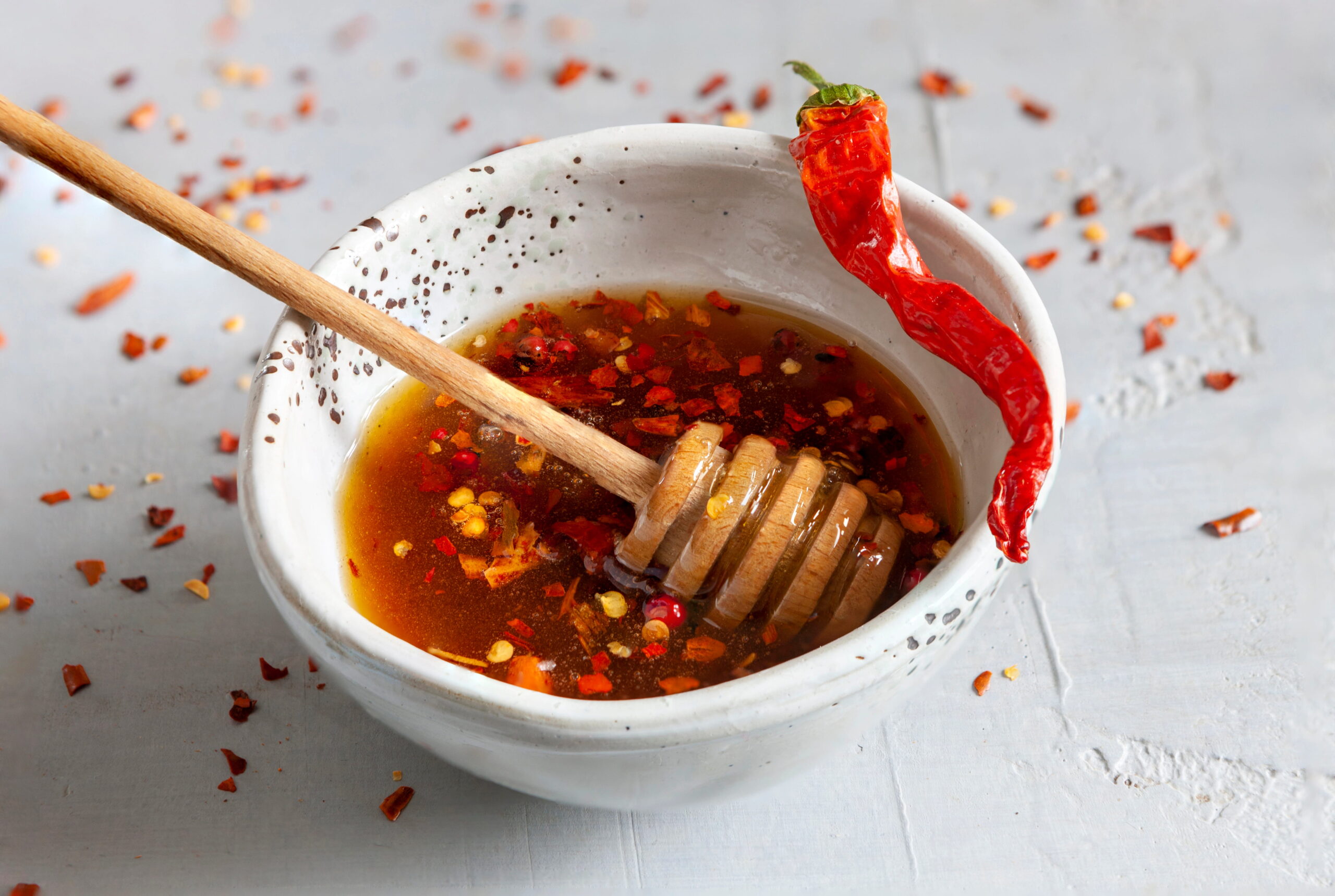 Small bowl of hot honey, pepper flakes, chili resting on edge of bowl