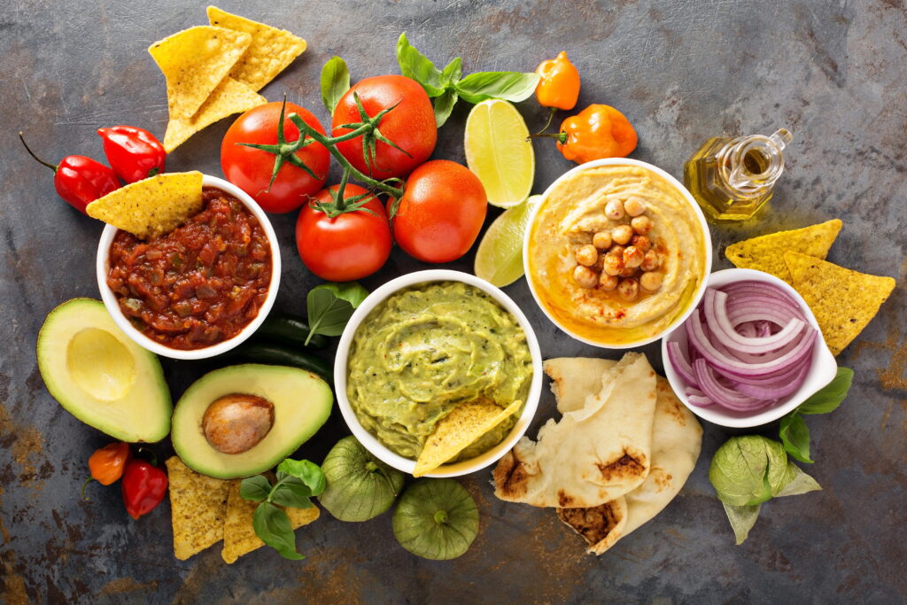bowls of salsa, guacamole, and hummus with assorted foods to dip
